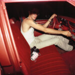A man at the wheel of a red car with a red interior. His face is hidden from sight.